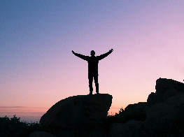 A man on a mountaintop raising his hands against the morning sky